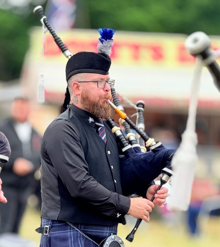 Pipe Major Rich Smith playing the bagpipes, in his uniform.